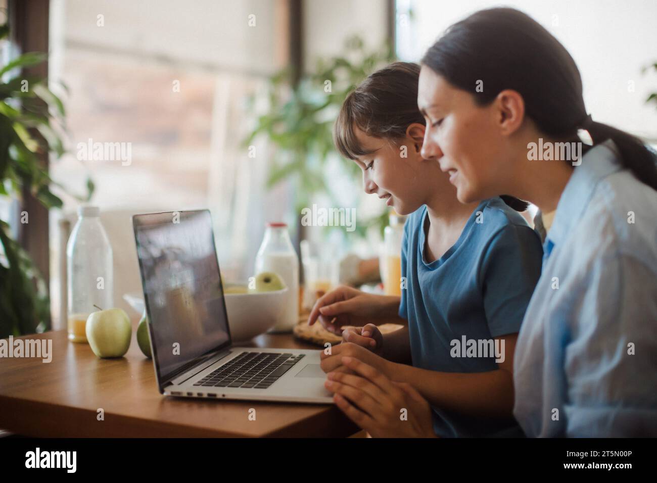 Mom and daughter watching entertaining videos on mom's work laptop. Remote work, home office for mothers with children. Stock Photo