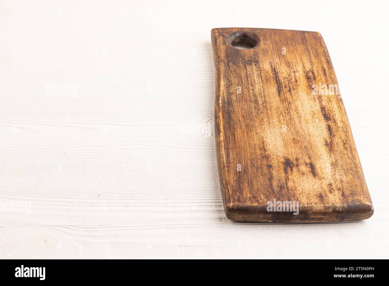 Empty rectangular wooden cutting board on white wooden background. Side view, copy space. Stock Photo