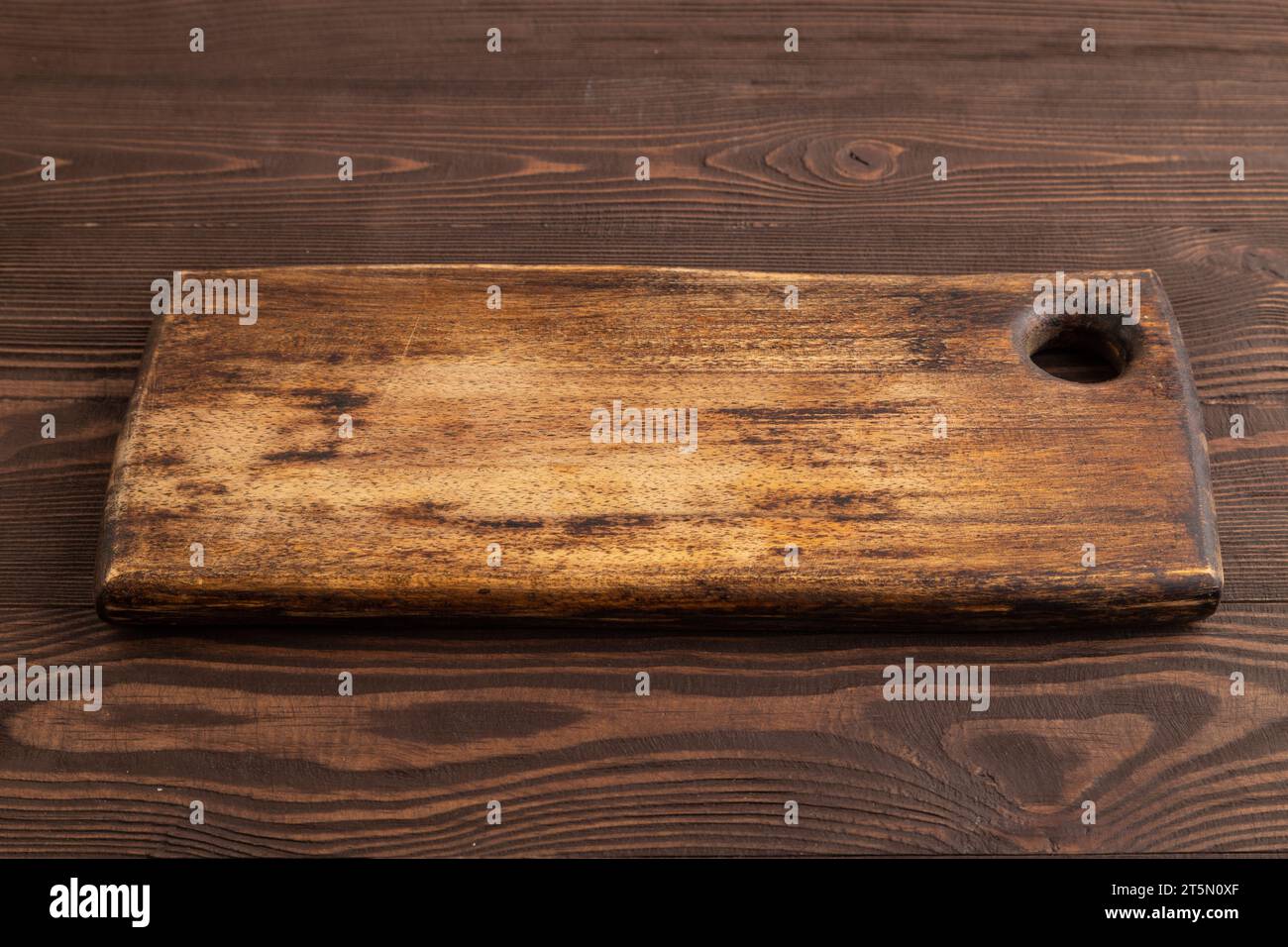 Empty rectangular wooden cutting board on brown wooden background. Side view, close up. Stock Photo