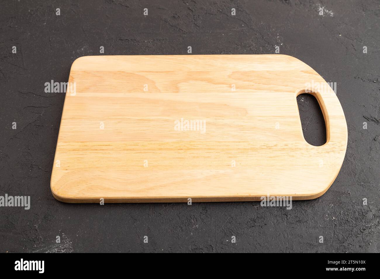 Empty rectangular wooden cutting board on black concrete background. Side view, close up Stock Photo