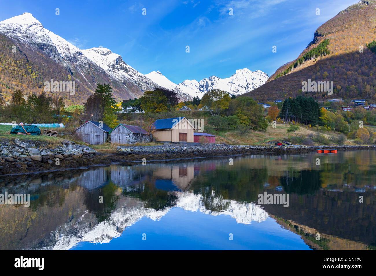 Stunning scenery with mountains & wooden huts reflected in water by Hjorundfjorden fjord at Urke, Norway, Scandinavia, Europe in October Sunnmøre Alps Stock Photo