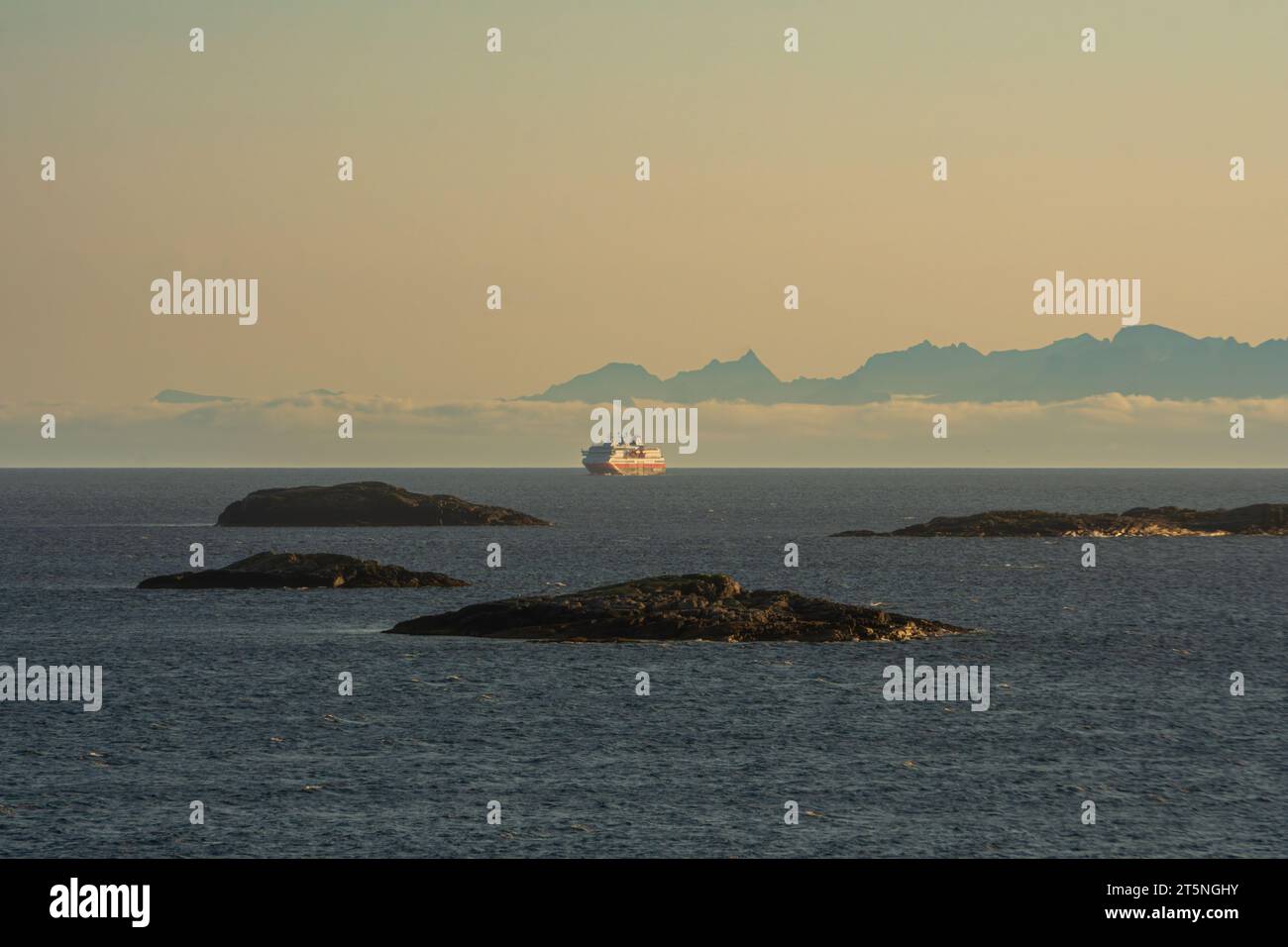 Cruise ship, Hurtigrutten, seen from afar, in Lofoten, Norway. High peaks in the background. Copy space. Stock Photo