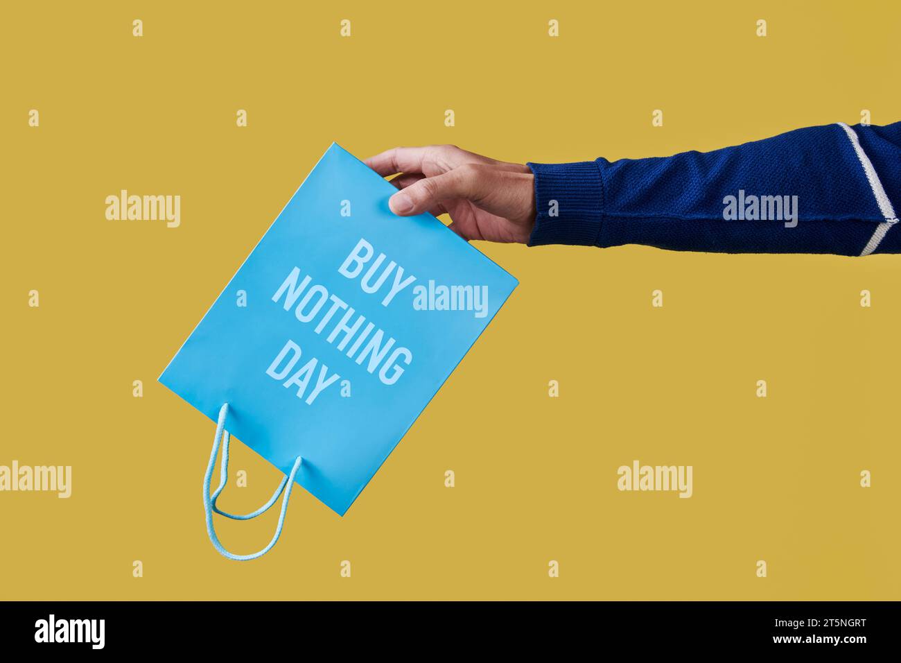 closeup of a man holding a blue shopping paper bag, with the text buy nothing day written in it, upside-down on a yellow background Stock Photo