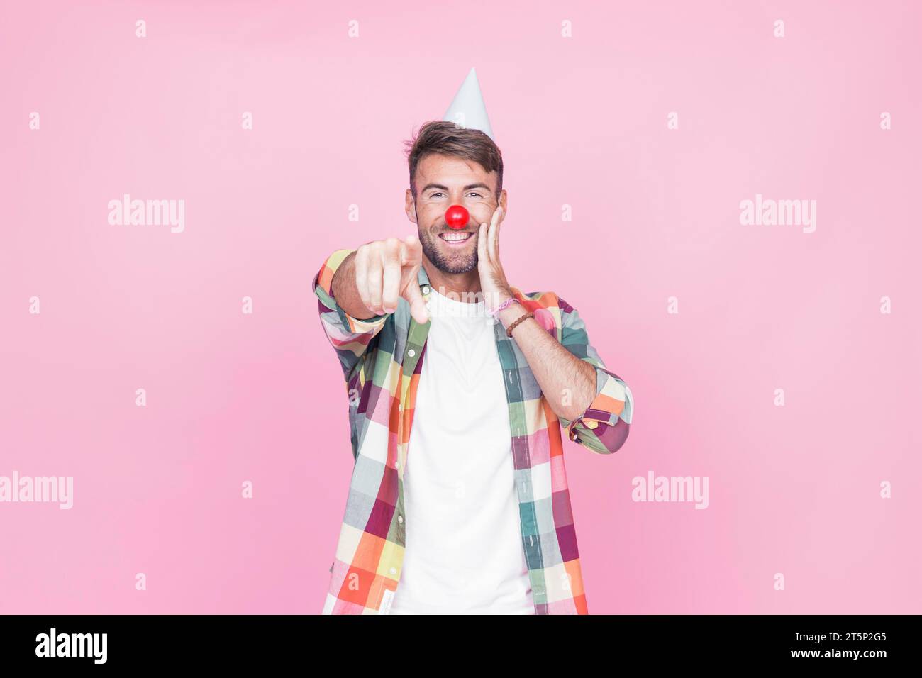 Young man with clown nose pointing his finger pink background Stock Photo