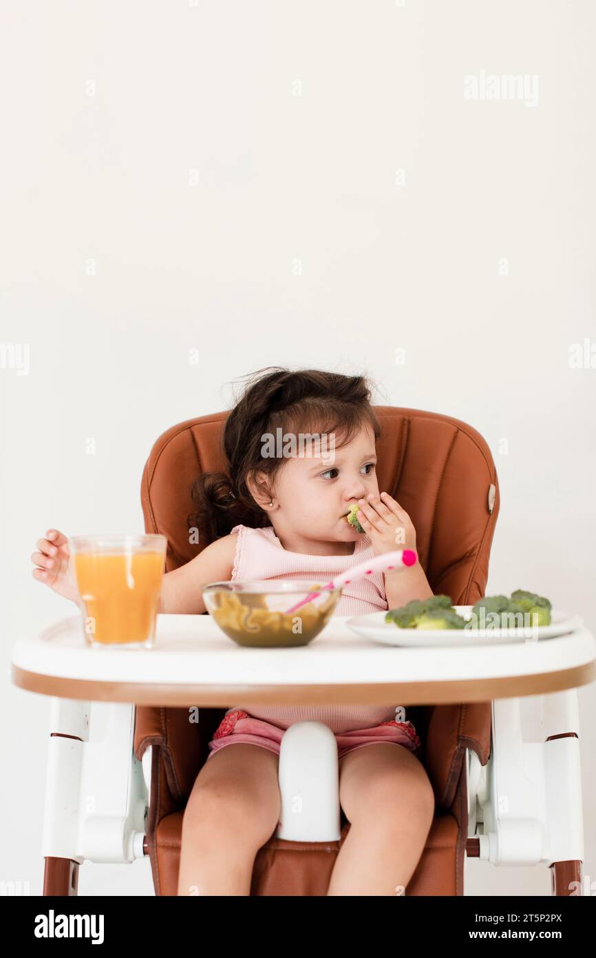 Baby girl eating child chair Stock Photo