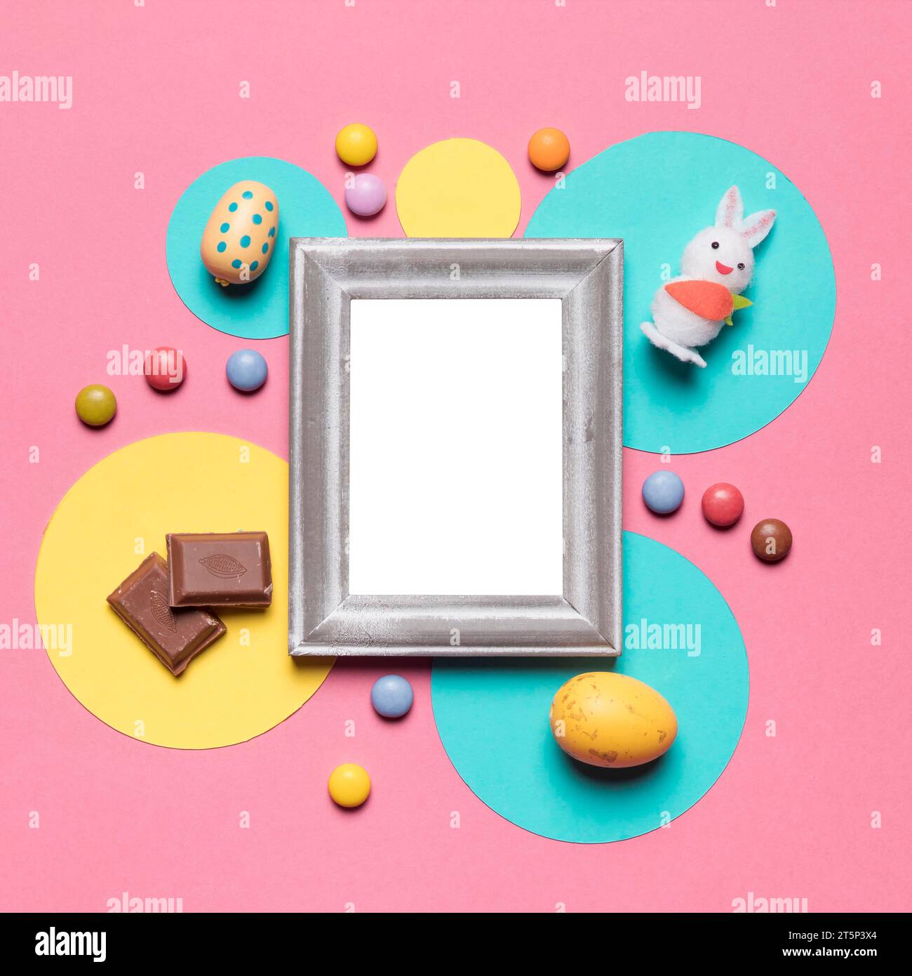 Empty frame surrounded with easter eggs bunny candies chocolate pieces pink backdrop Stock Photo