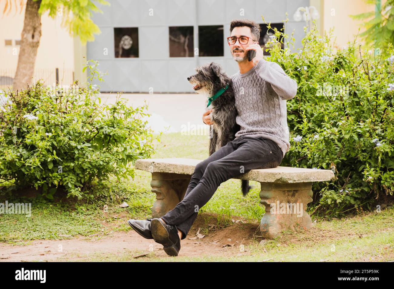 Modern man sitting park with his dog talking mobile phone Stock Photo