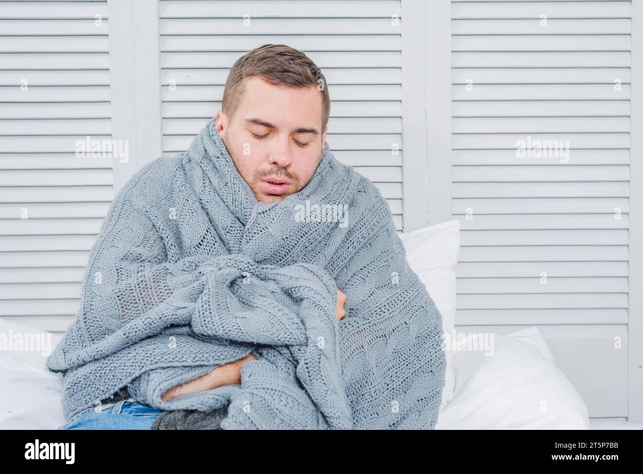 Young man wrapped warm scarf shivering from cold Stock Photo