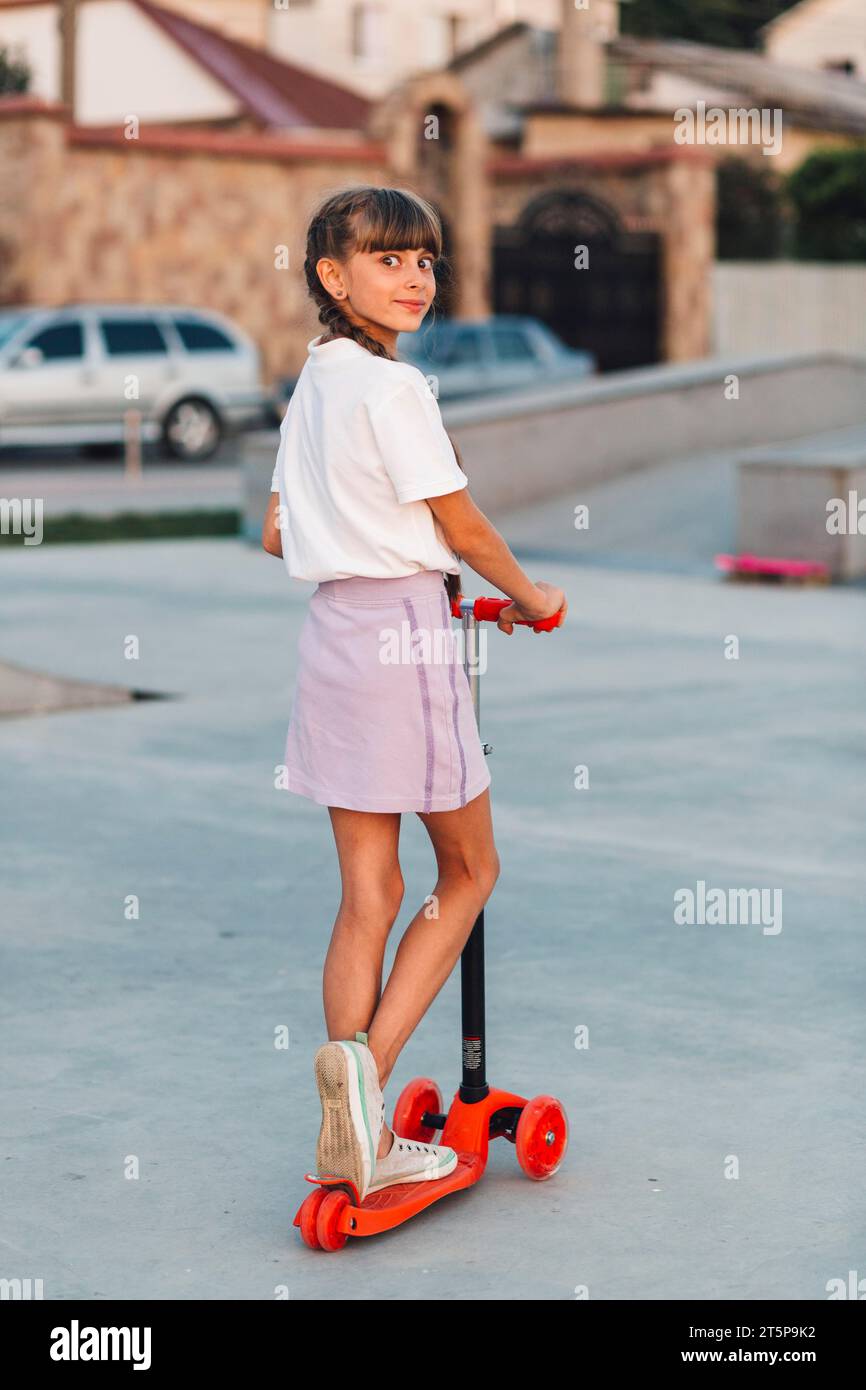 Smiling girl standing push scooter looking back Stock Photo