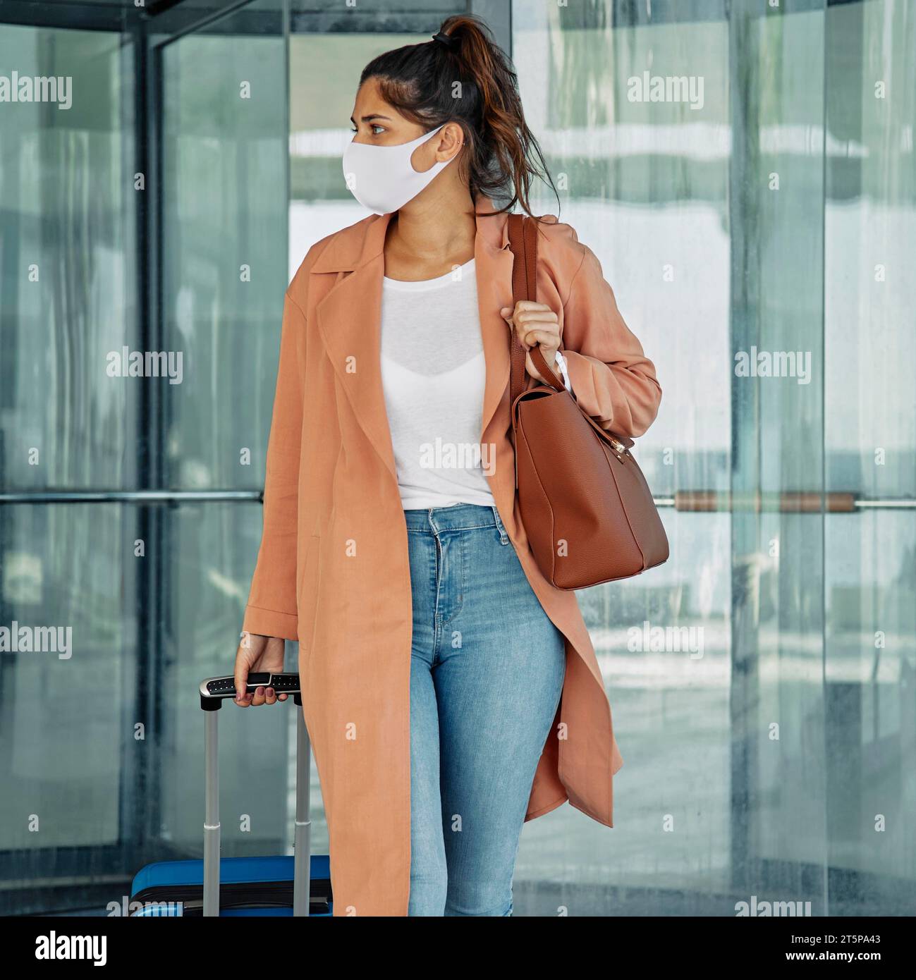 Woman with medical mask carrying luggage airport during pandemic Stock Photo