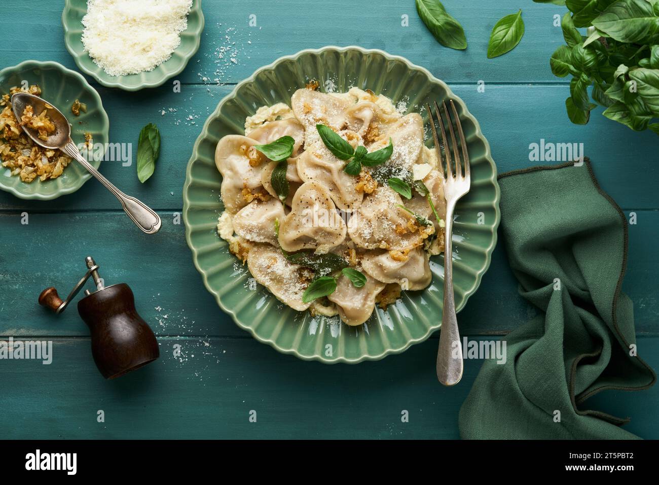 Homemade italian ravioli pasta in heart shape with beef meat, cheese sauce, caramelized onions, basil and saffron on old wooden blue background. Food Stock Photo