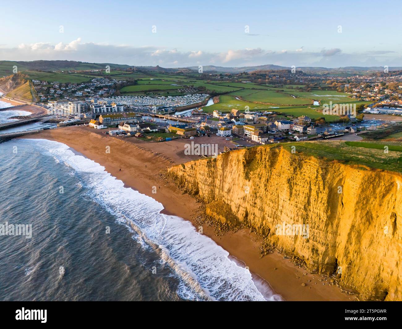 West Bay, Dorset, UK.  6th November 2023.  UK Weather.  Aerial view of the beach and cliffs at West Bay in Dorset which glow golden yellow in the late afternoon autumn sunshine shortly before sunset, after a day of heavy showers.  The beach and cliffs took a battering during Storm Ciaran which flooded a beach cafe and led to a large cliff rockfall.  Picture Credit: Graham Hunt/Alamy Live News Stock Photo