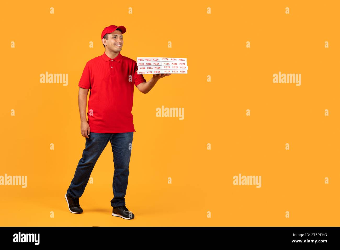 courier guy in uniform presents takeaway pizza boxes, yellow backdrop Stock Photo