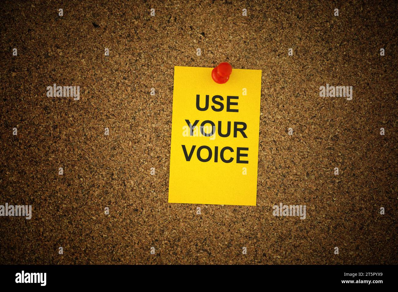 A yellow paper note with the slogan Use Your Voice on it pinned to a cork board. Close up. Stock Photo