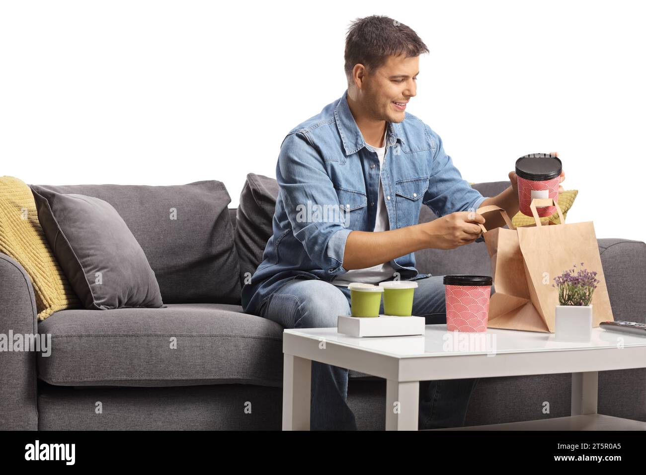 Man smiling and sitting on a sofa with delivery food on a table Stock Photo