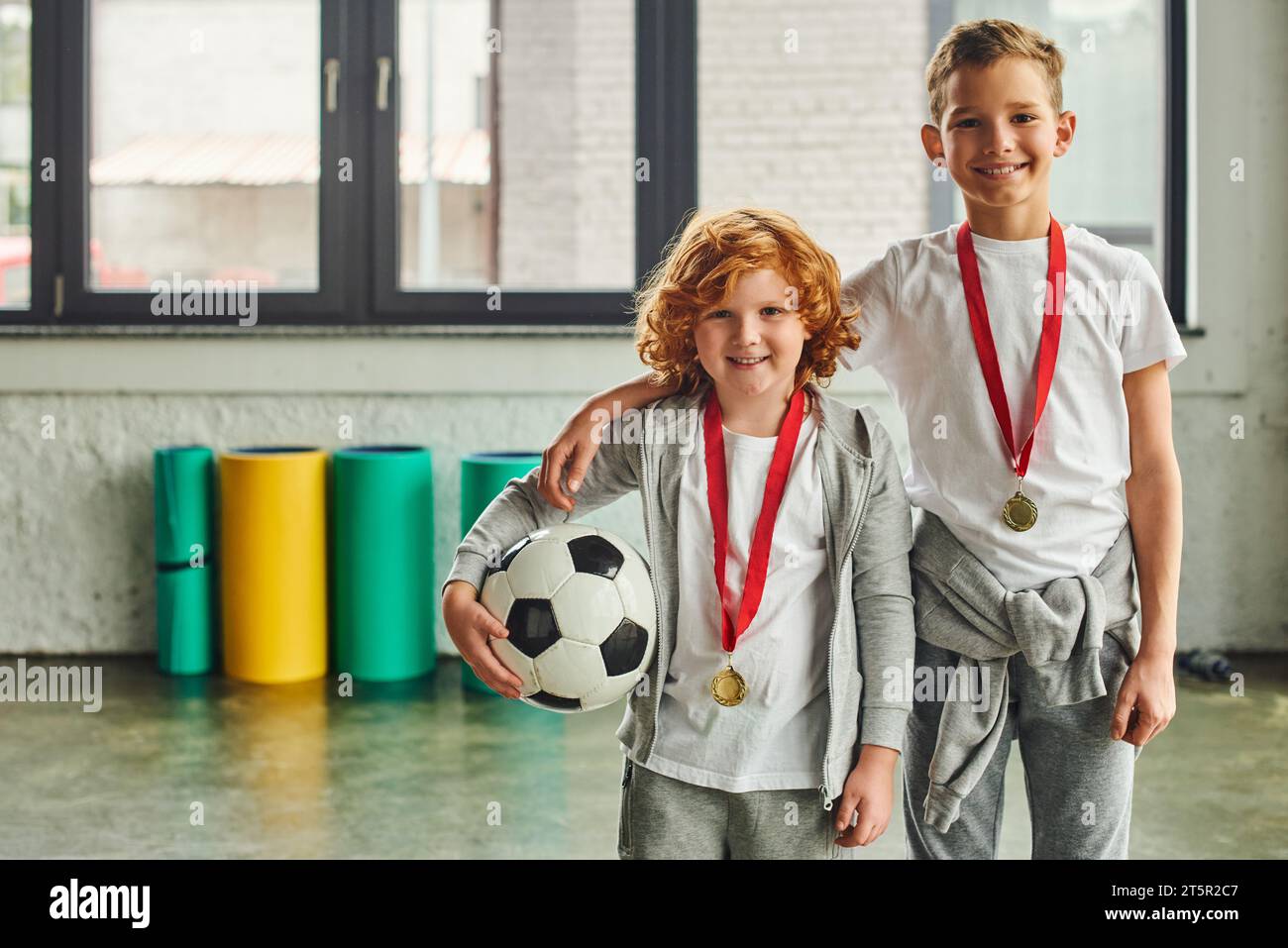 two cheerful boys in sportswear with golden medals holding soccer ball and smiling at camera, sport Stock Photo