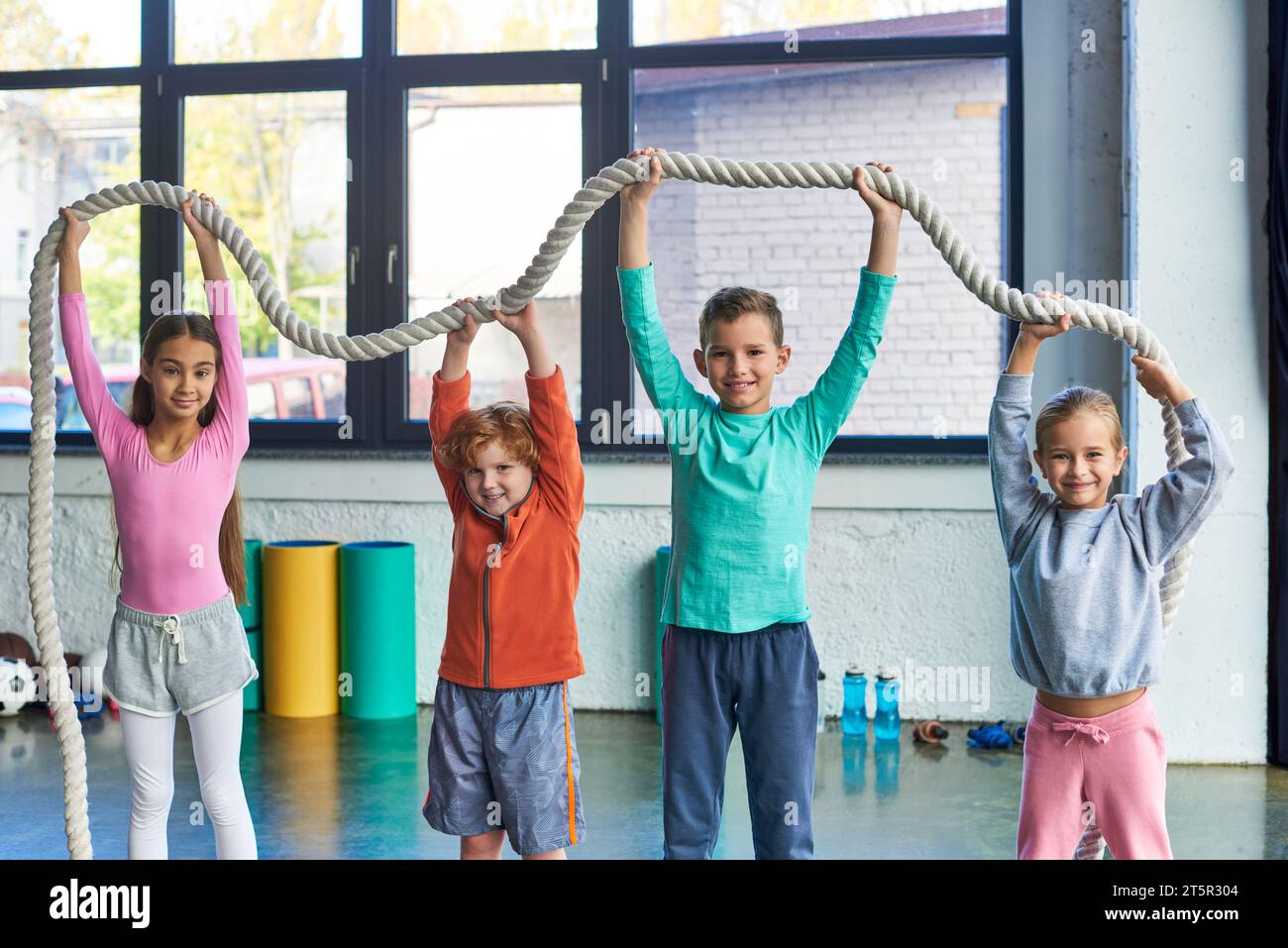 Children Exercise Rails four little cute children in sportswear raising fitness rope above ...