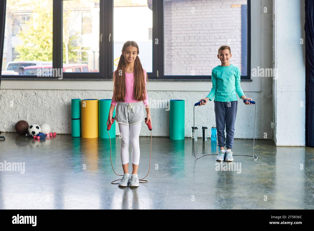 little cute boy and girl in sportswear posing with jump ropes and ...