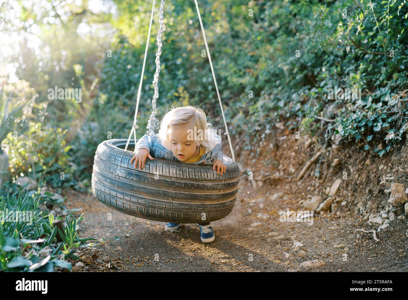 Little girl swings on a tire swing, leaning on her belly Stock Photo