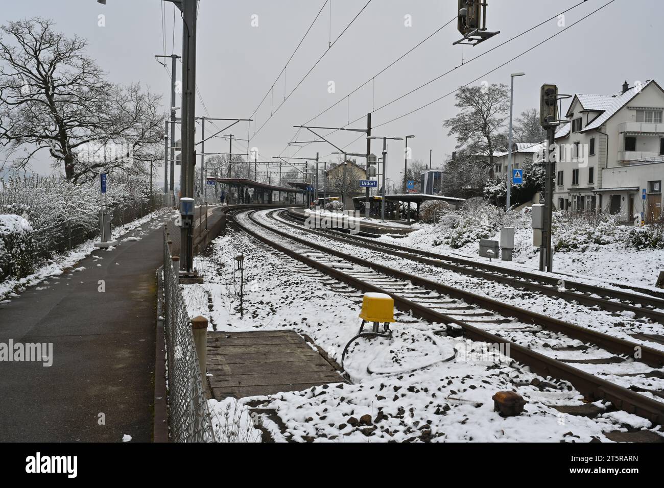 Sidewalk to railway platform and rails of a small village station Urdorf, Switzerland in winter. Stock Photo