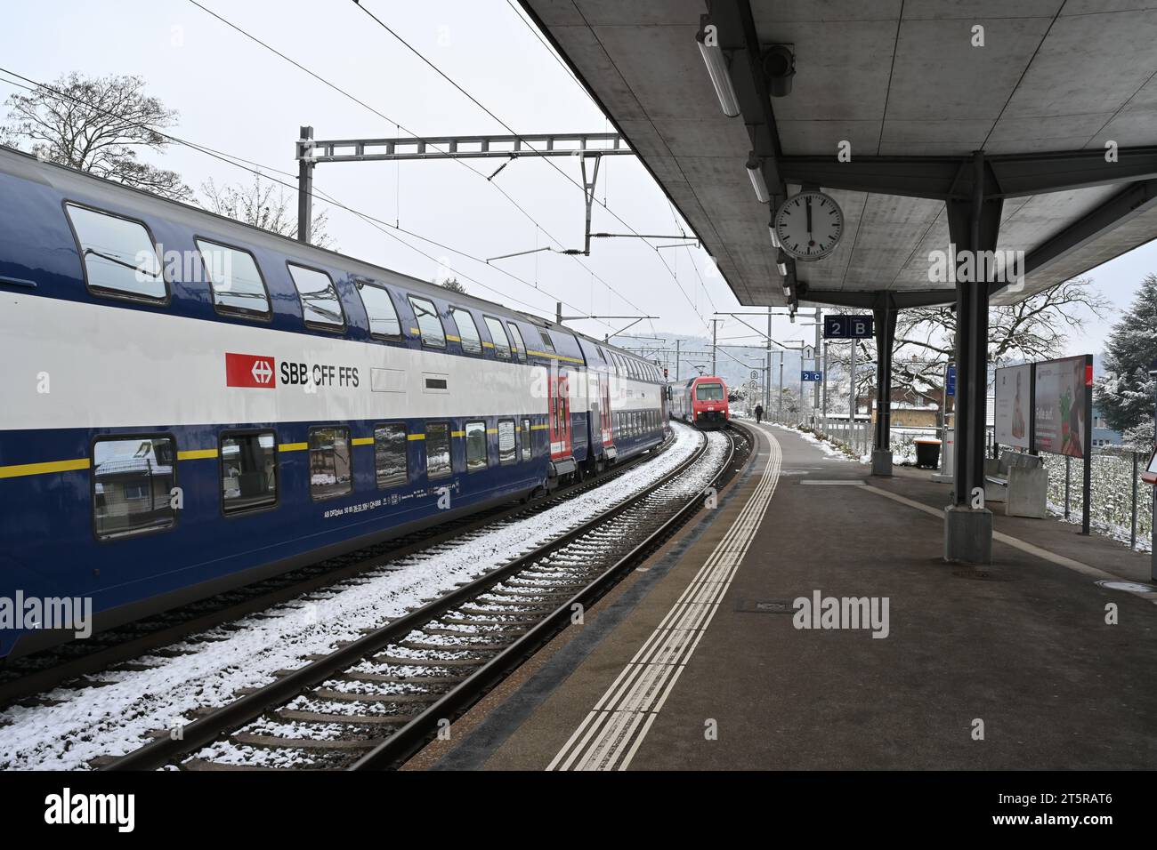 Two local passenger trains with wagons arriving to railway platform of a small village station  in Urdorf, Switzerland in winter. Stock Photo