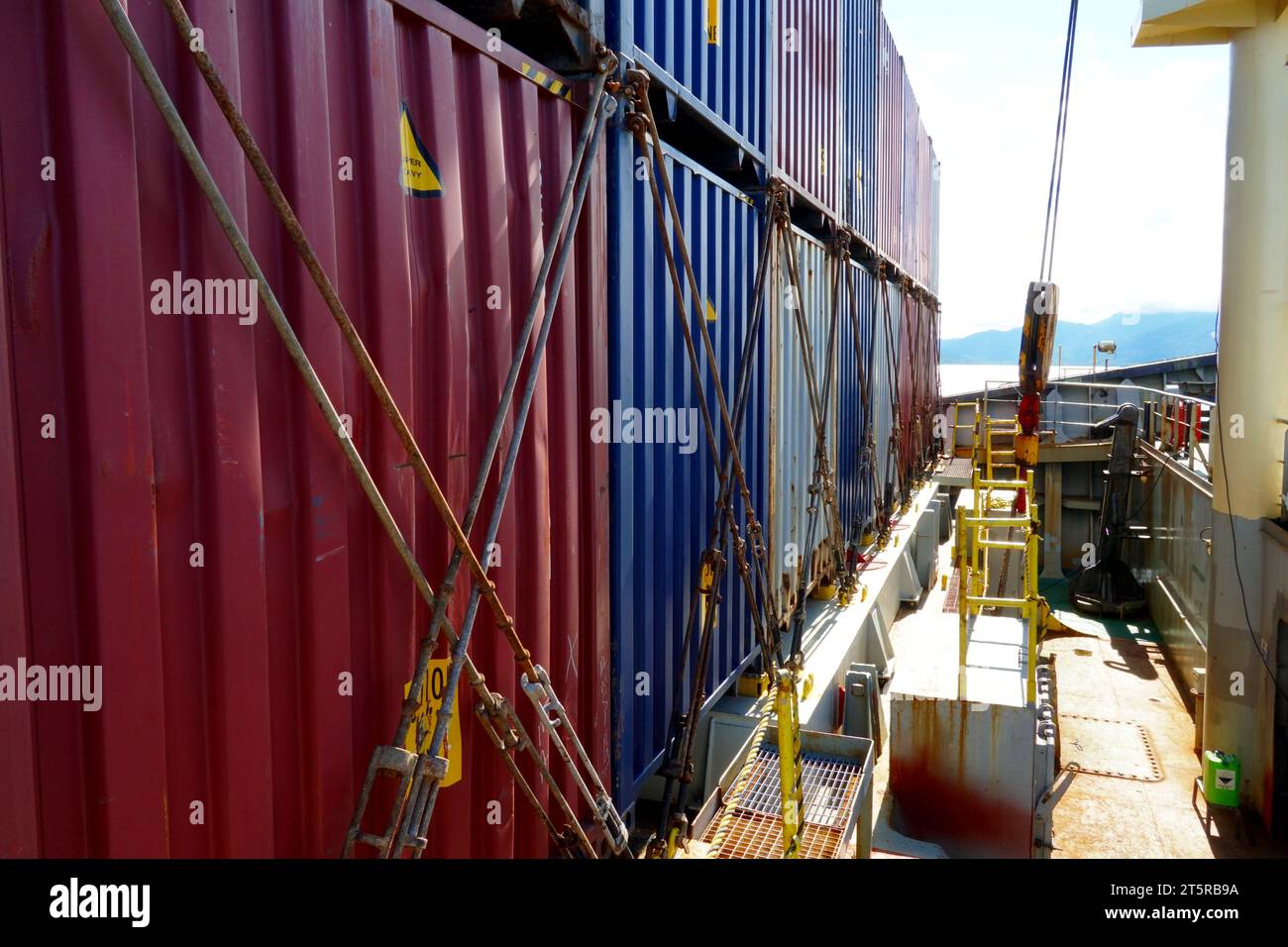 Row of lashed containers in a line with bars and twist locks situated in forward of container vessel with cranes. Stock Photo