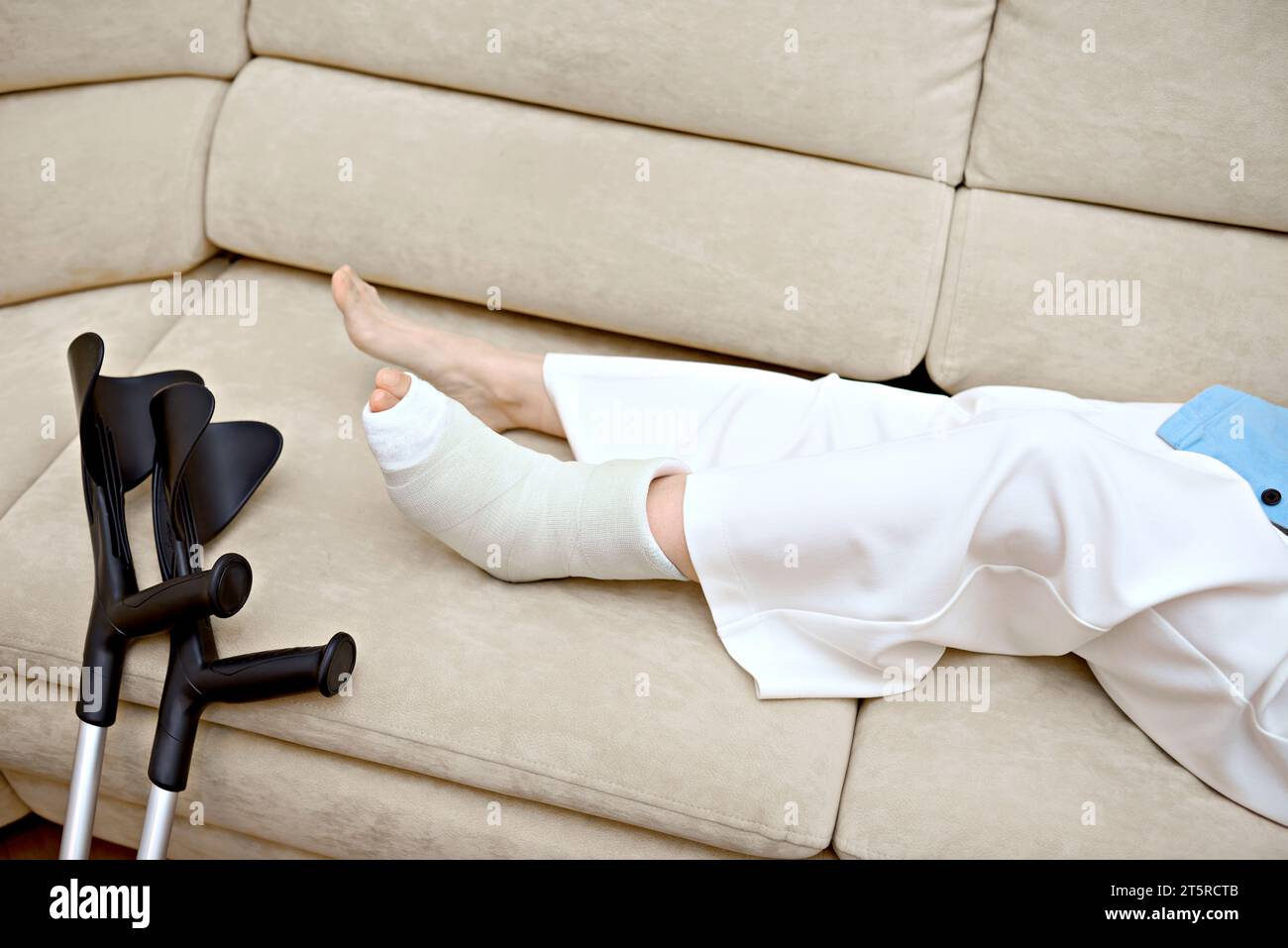 Young female with leg bone fracture resting on couch at home. Serious physical accident injury.  Rehabilitation concept for individuals injured Stock Photo
