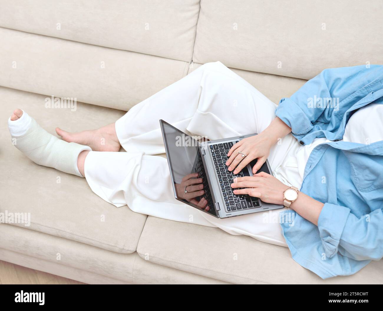 A lady with broken foot  consulting with doctor online using her laptop. Idea of telemedicine for online patient counseling. Woman seeking remote work Stock Photo