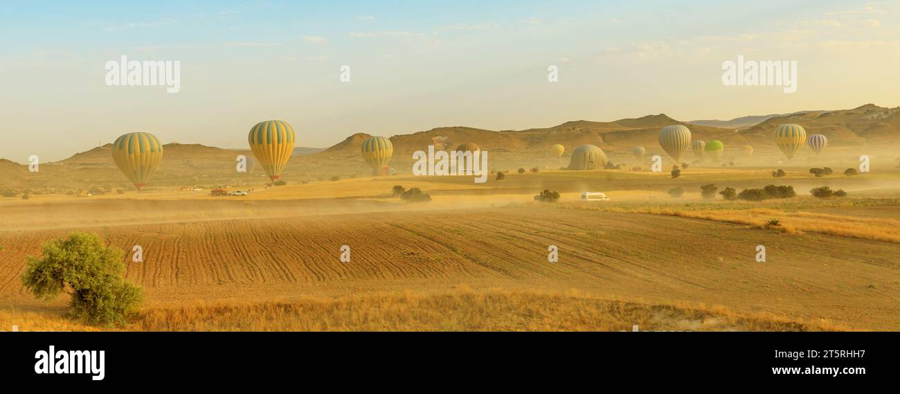 landscape panorama of the hot air balloons of Cappadocia ascend into the sky at dawn. Against the backdrop of a warm and dusky atmosphere above Goreme Stock Photo