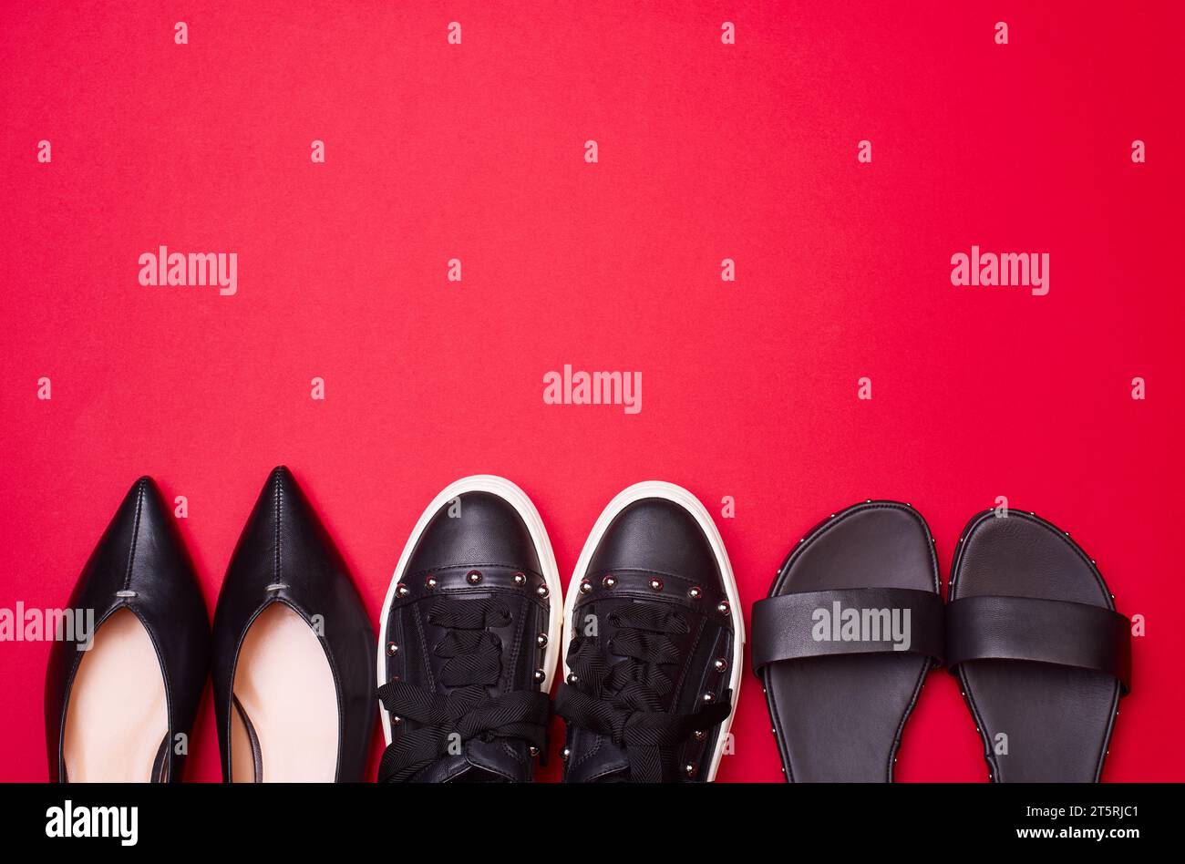 Variety of modern black women's shoes on a bright reddish pink background with copy space. Stylish pumps, sneakers and sandals. Flat lay, top view. Mo Stock Photo