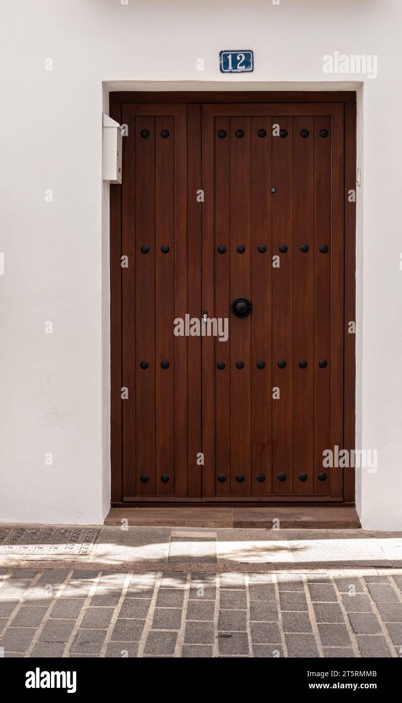 Old Fashioned style dark wooden door with metal studs set in a white wall Stock Photo