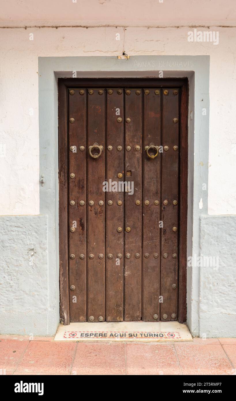 Old Fashioned style dark wooden door with metal studs set in a white wall Stock Photo