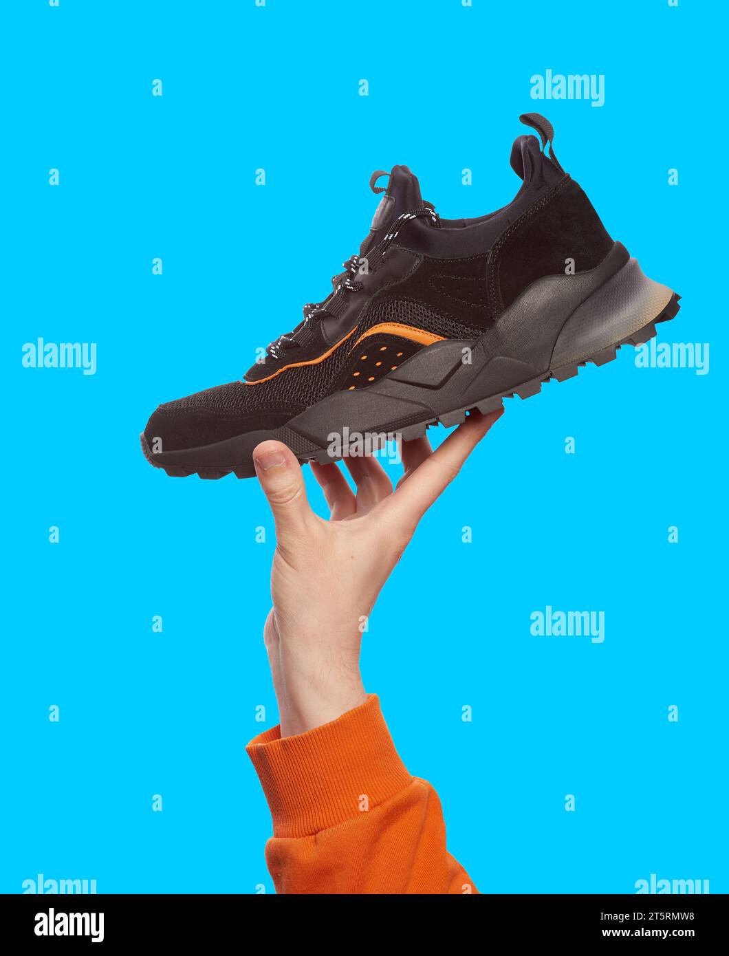 Stylish black sneaker with chunky sole in man's hand, isolated on a bright blue background. Mock-up for advertising a sports footwear shop Stock Photo