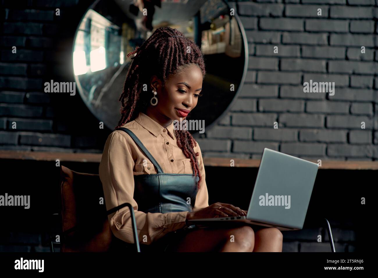 Attractive black woman sitting in a modern office and typing on a laptop. Young entrepreneur doing work. Woman consultant with remote work, online man Stock Photo