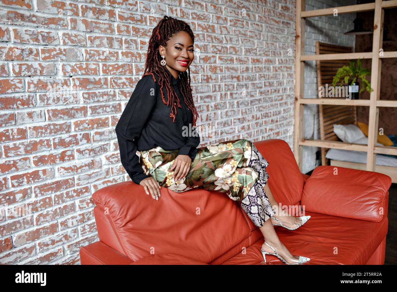 Attractive African woman smiling sitting on the back of the red leather ...