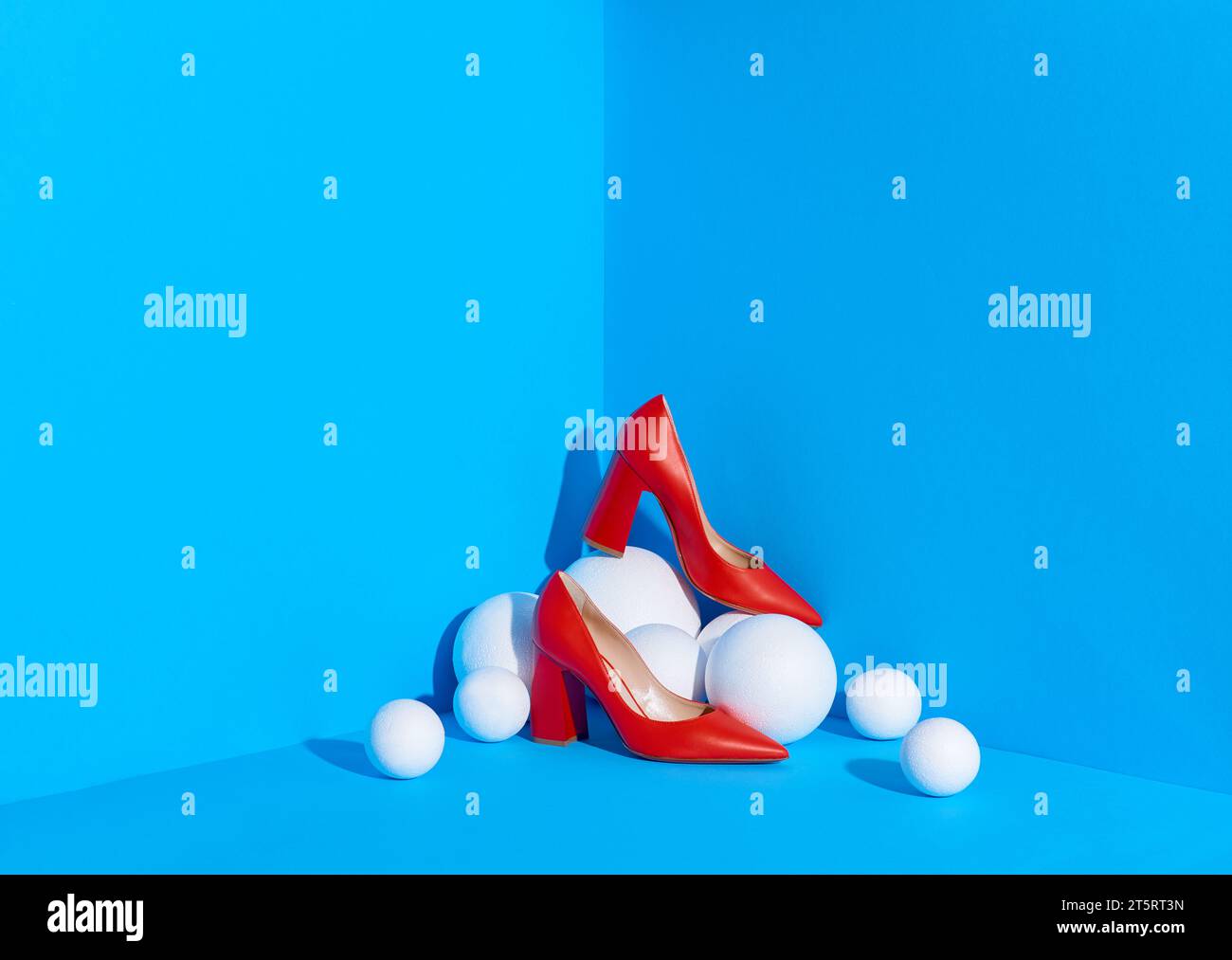 A studio shot of classic red women's shoes placed in the corner of blue-colored space on white spheres. Fashion blog or magazine concept. Copy space. Stock Photo