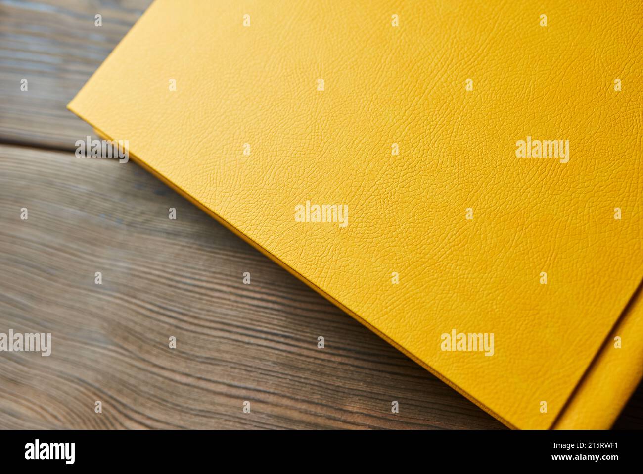 A cropped shot of a yellow-covered book isolated on a wooden background. Close-up, top view. Studying, journaling or reading. Stock Photo