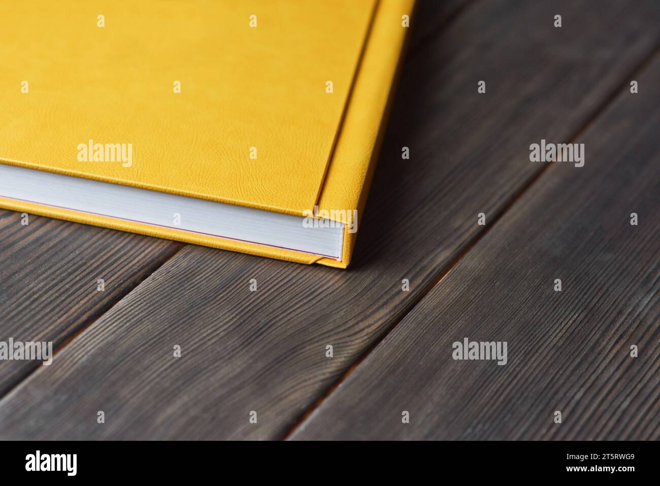 A cropped image of thick book with yellow textured hardcover isolated on a wooden desktop with copy space for text. Mock-up for blog Stock Photo