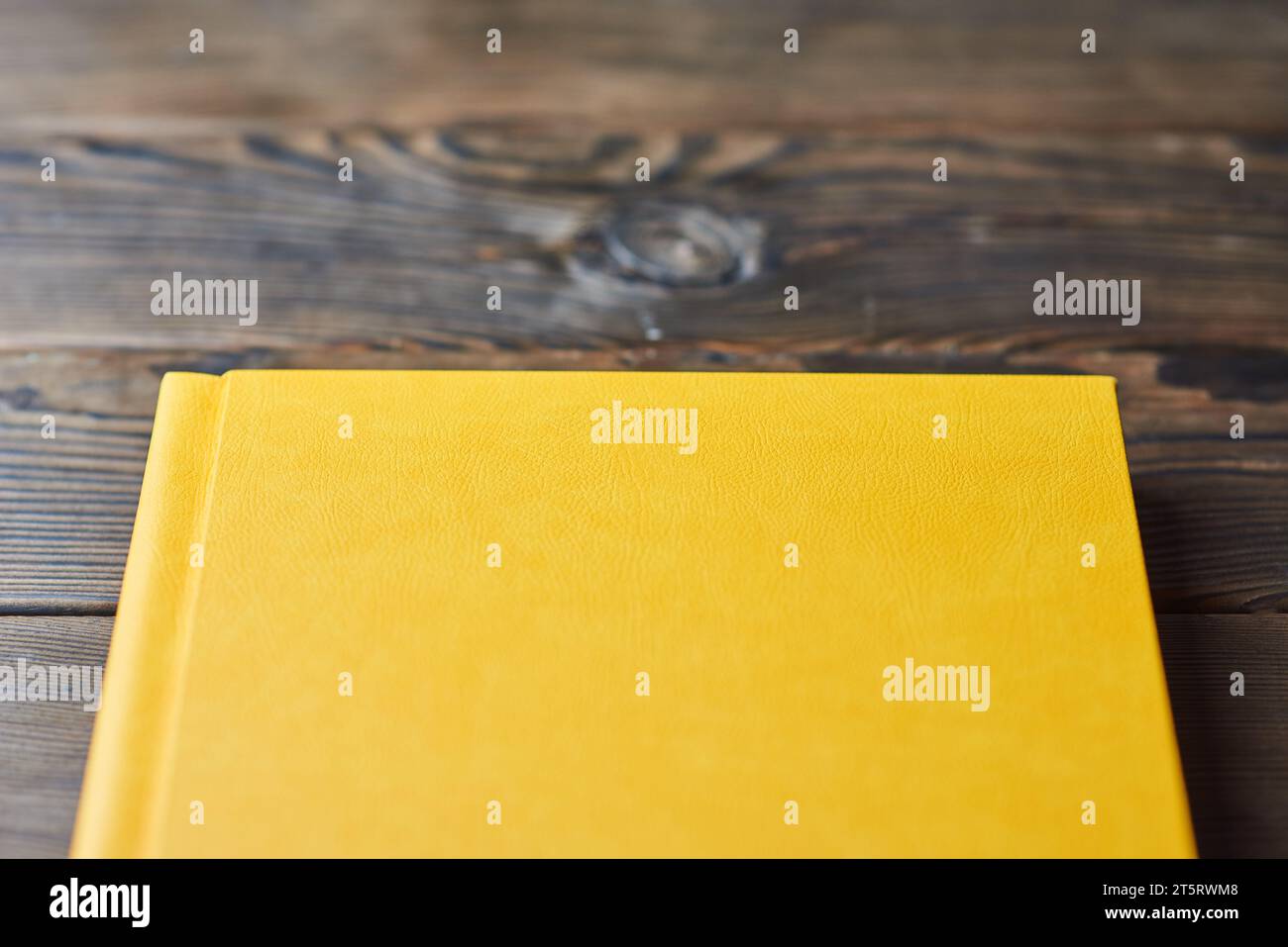 Book with yellow leather hardcover isolated on a brown wooden background. Closeup, first-person POV. Book, photo album, diary, planner or scrapbook is Stock Photo