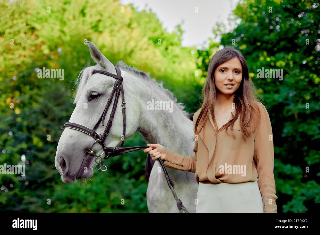 Young jockeygirl leads a saddled brown horse by the reins.Horse school