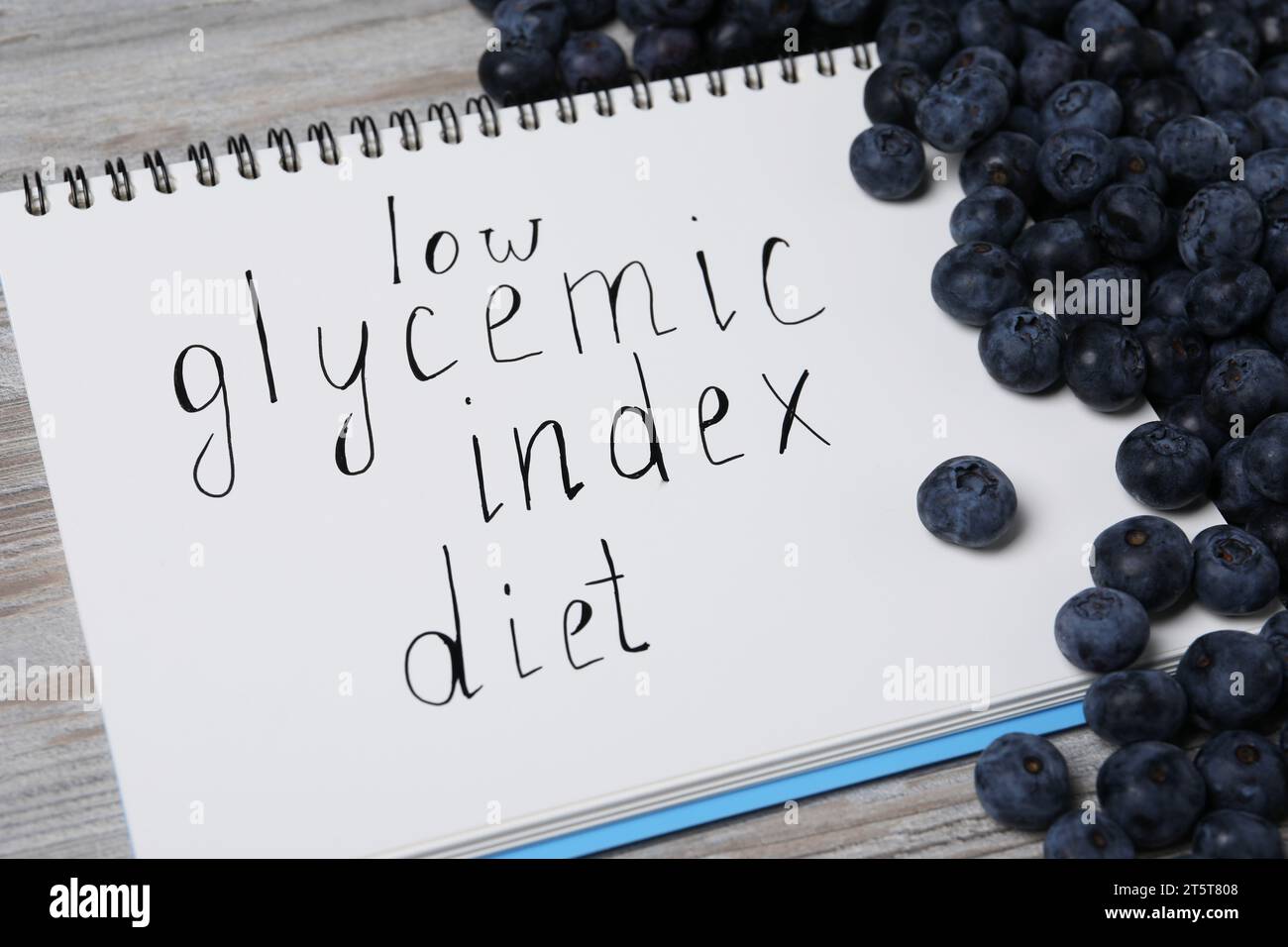 Notebook with words Low Glycemic Index Diet and blueberries on light wooden table, closeup Stock Photo