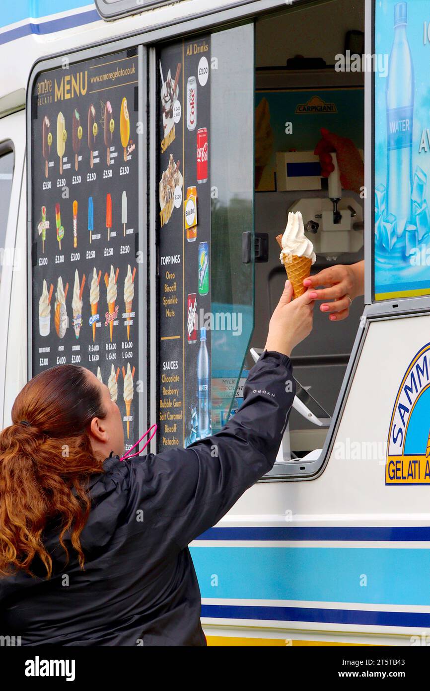 A happy customer accepts a freshly made 99 Flake ice cream by the vendor at the serving counter of an ice cream van during a busy local food festival. Stock Photo