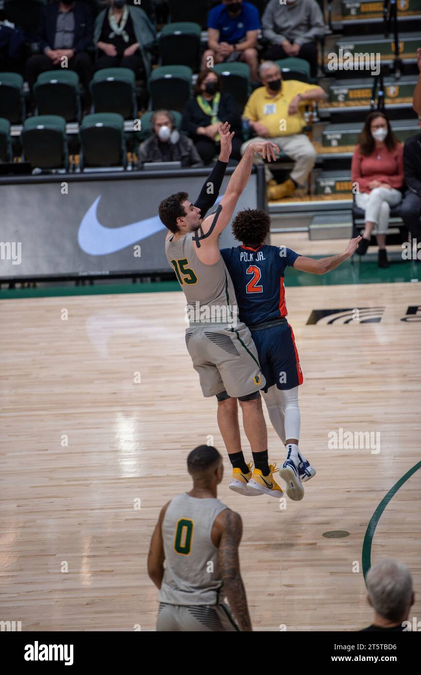 College basketball player taking a contested jump shot during NCAA game ...