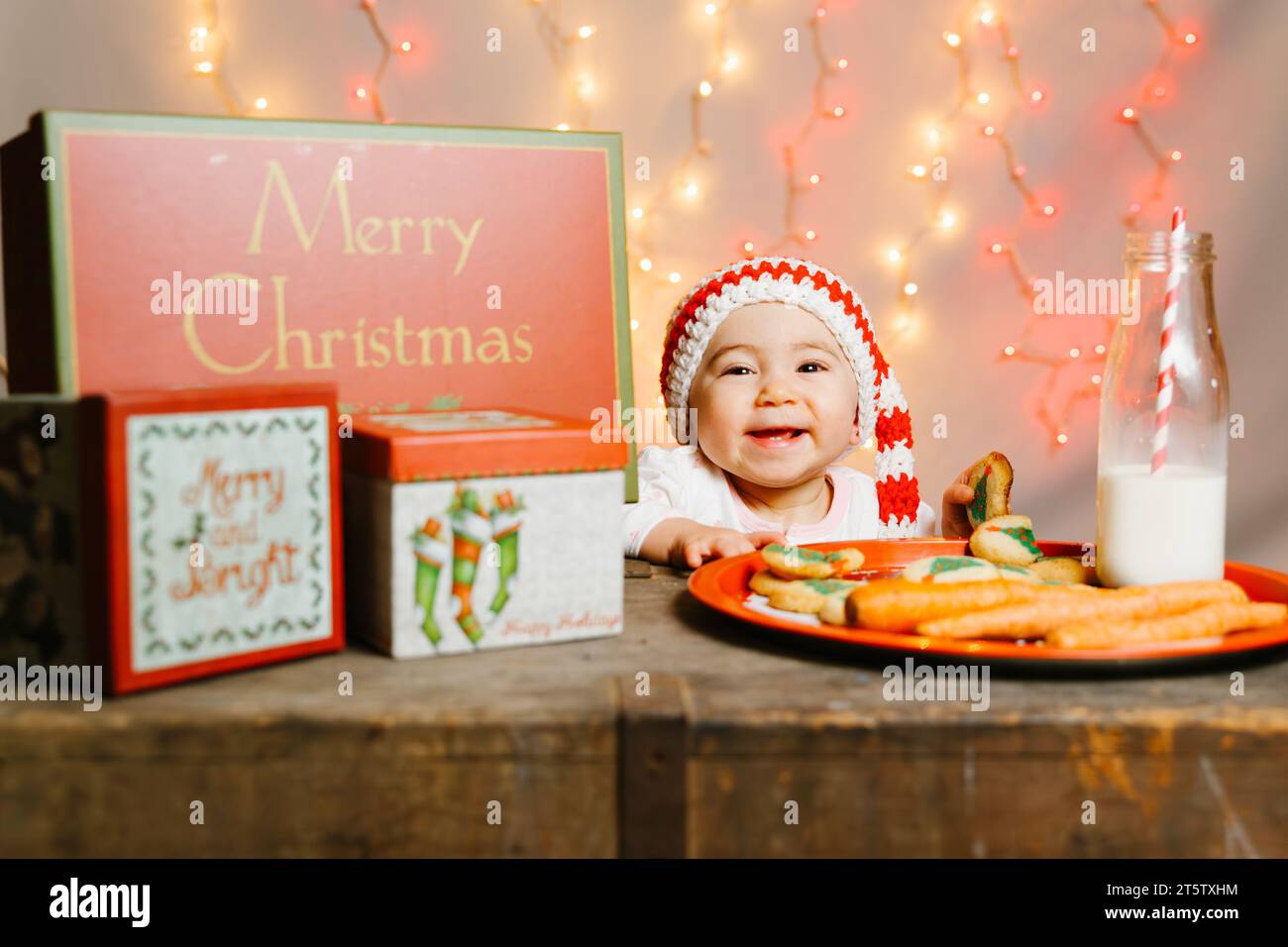 Awaiting Santa Baby with Knit Hat Among Gifts and Treats Christmas Eve Stock Photo
