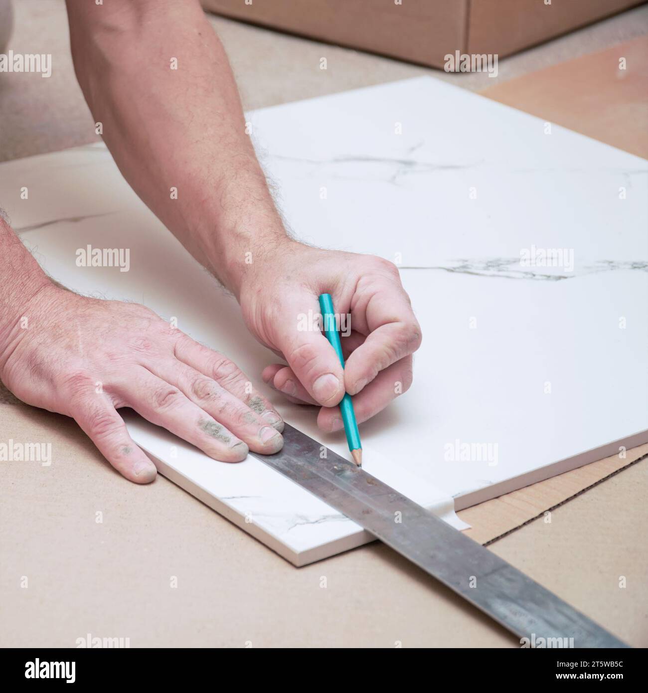 The hands of a man marking ceramic floor tiles with a ruler and pencil ...