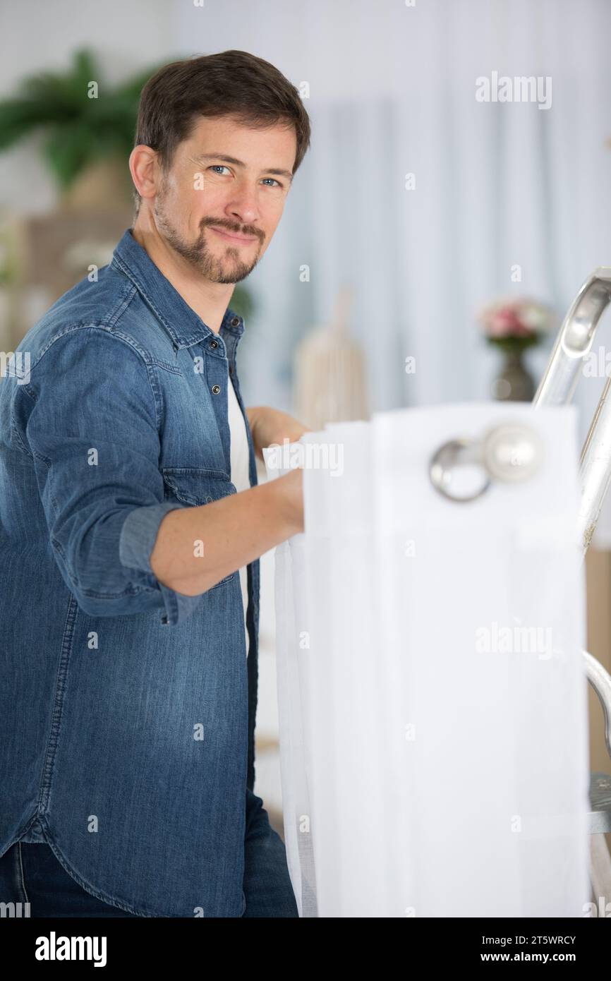 young man installing curtains over window Stock Photo