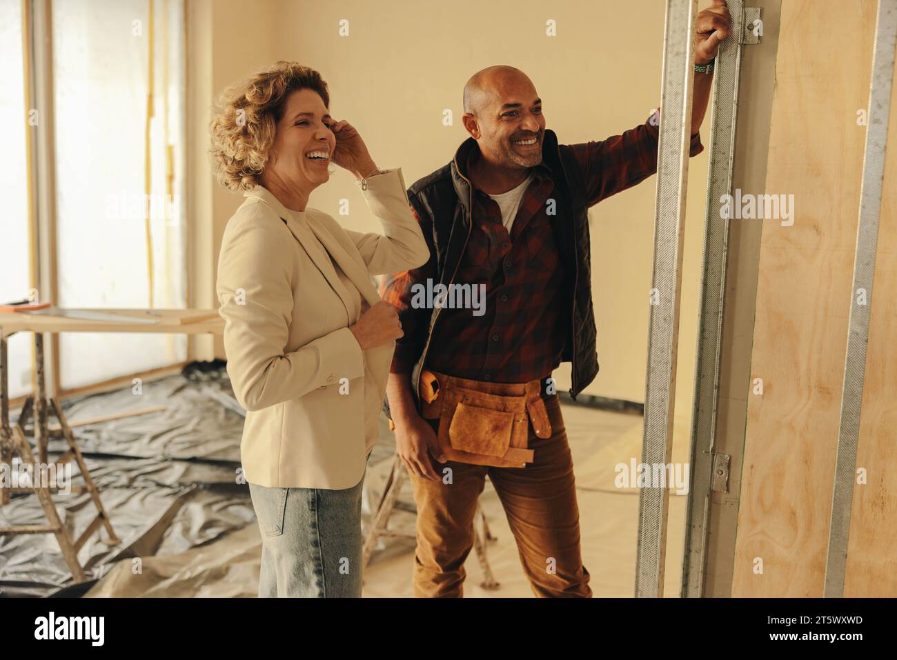 Male builder and female architect collaborate on a home renovation project. They discuss the remodel inside a house, near a doorframe. The contractor' Stock Photo