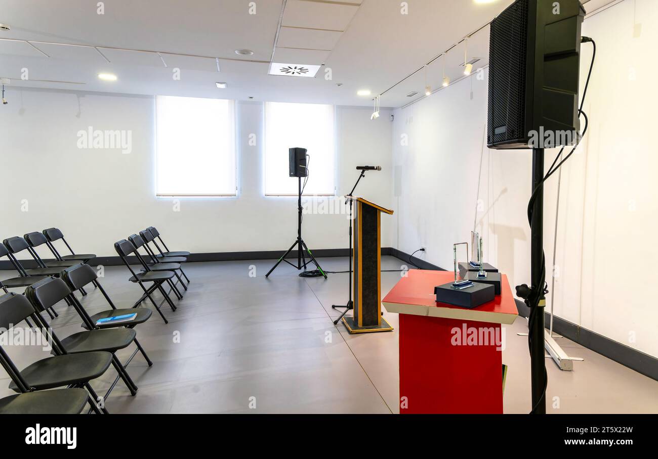 Modern and luminous room, empty, prepared for an event. Lectern with microphone and sound system and empty chairs to accommodate attendees Stock Photo