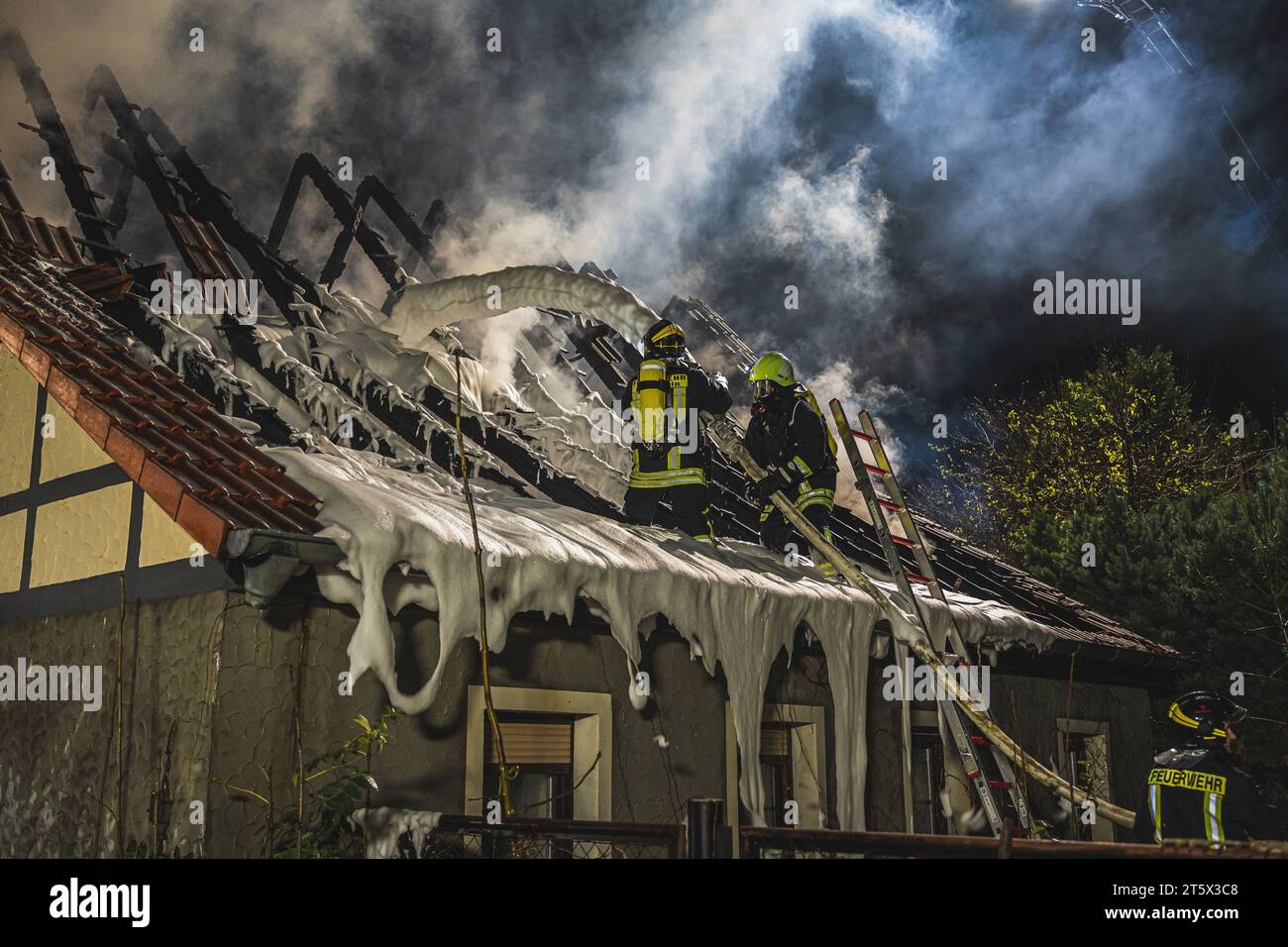 Zwei Einsatzkräfte der Feuerwehr bekämpfen einen Dachstuhlbrand mit Löschschaum. Rauch steigt aus dem völlig zerstörten Dach auf.  Am 06.11.2022 Stock Photo