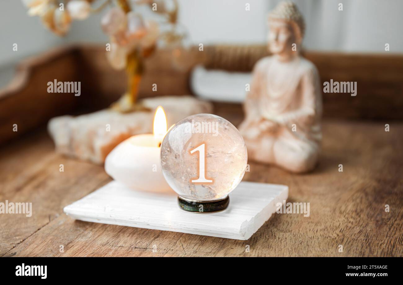 Number one on Gemstone sphere or crystal balls known as crystallum orbis and orbuculum. Natural clear quartz ball on stand on wood tray in home. Stock Photo
